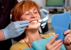 An older woman admiring her dentures while looking in a hand mirror