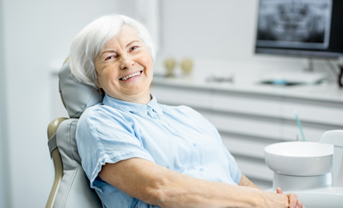 Senior female dental patient sitting in treatment chair smiling