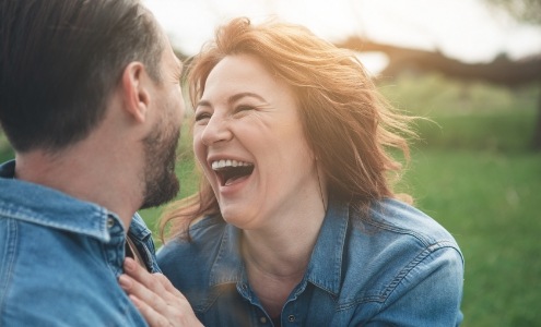 Man and woman smiling outdoors enjoying the benefits of dental implants