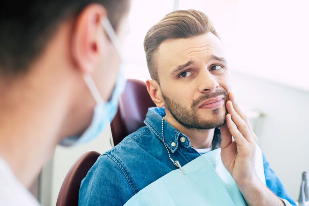 A man in a dentist's chair holding his jaw in pain.