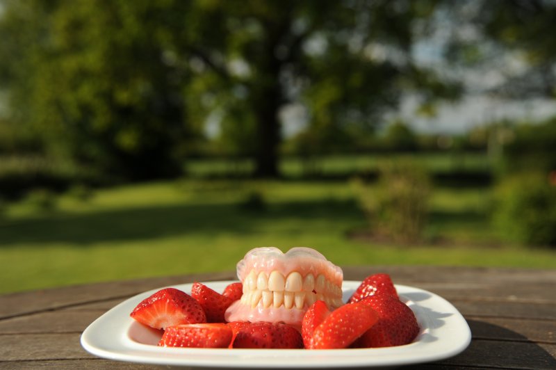 Two full dentures sitting on a plate full of strawberries